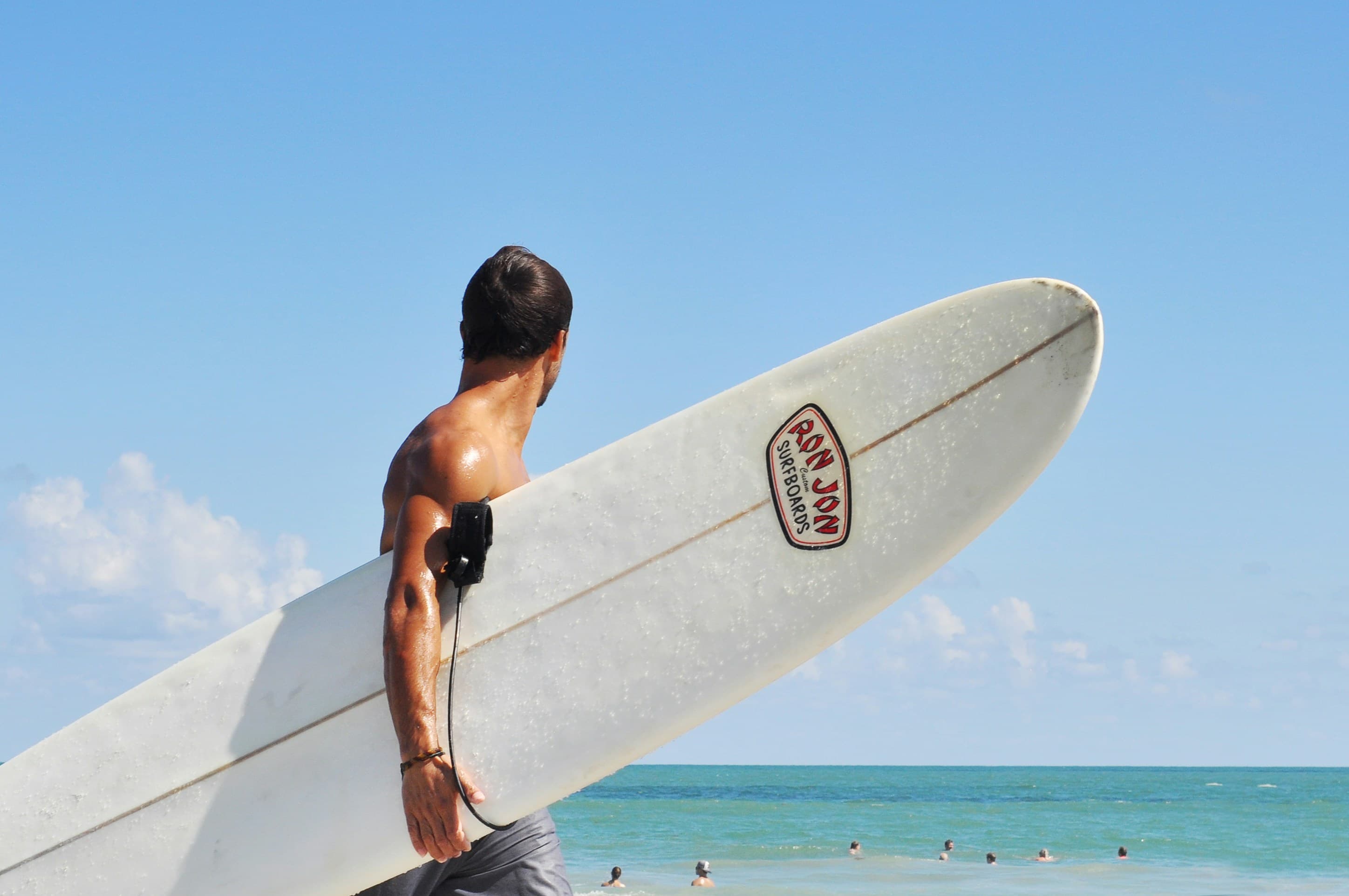 Surfer carrying a white surfboard along the beach